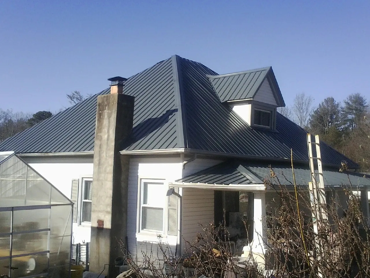 Dark blue standing seam metal roof on a white farmhouse with dormer — Slate & Tile Roof Repair by Roofing Brothers in Hasty
