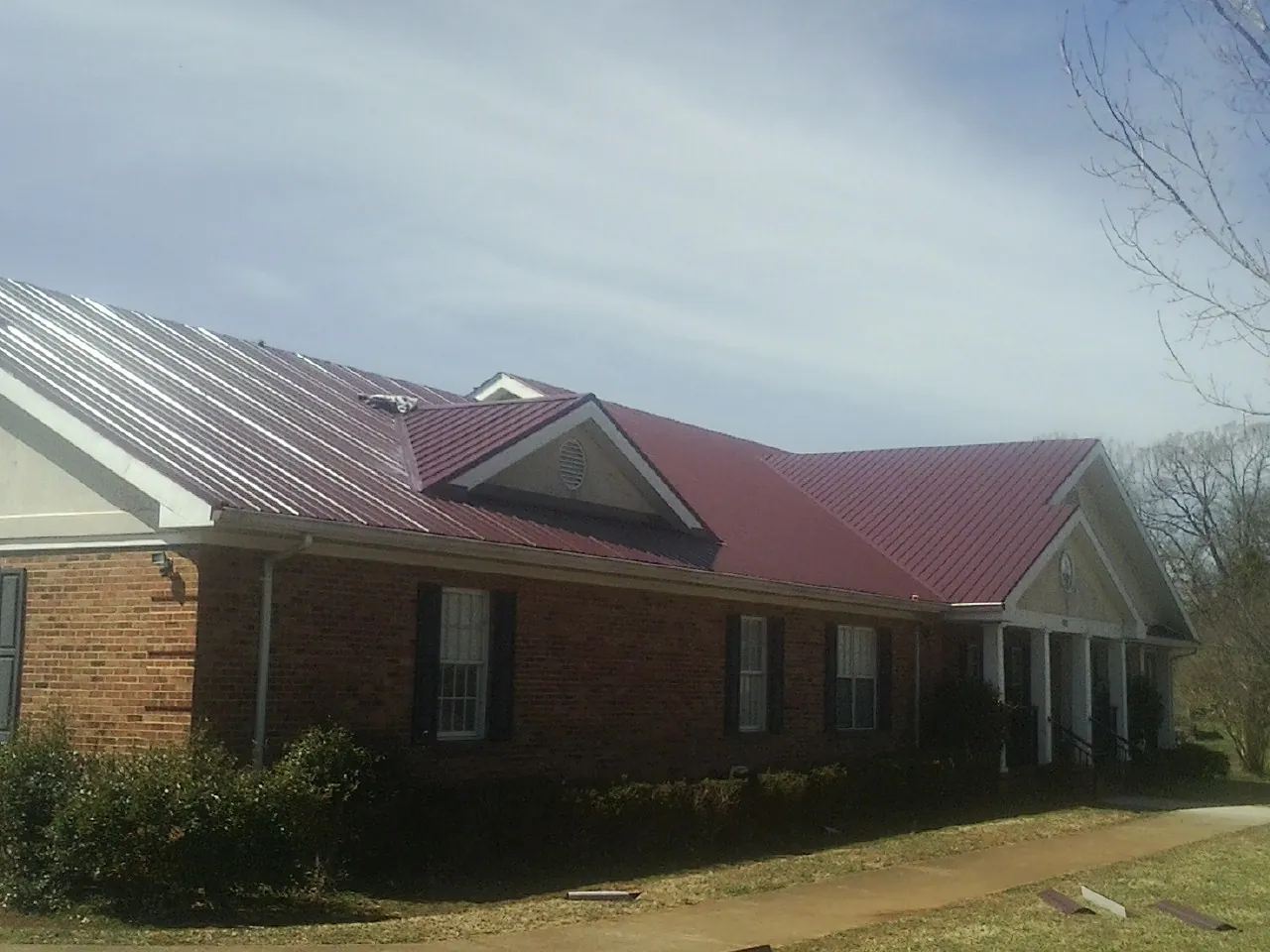 Red metal roof with gabled entries on a long brick building, from a Hail Damage Roof Repair job in Hasty