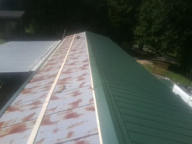 Old rusted panels beside newly installed green metal roofing — Wind Damage Roof Repair by Roofing Brothers in Hasty