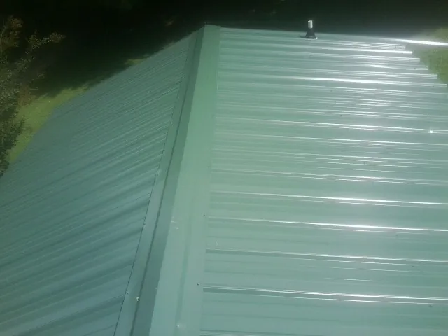 New green metal panels meeting at the ridge of a roof — Flat Roof Repair work by our crew in Hasty