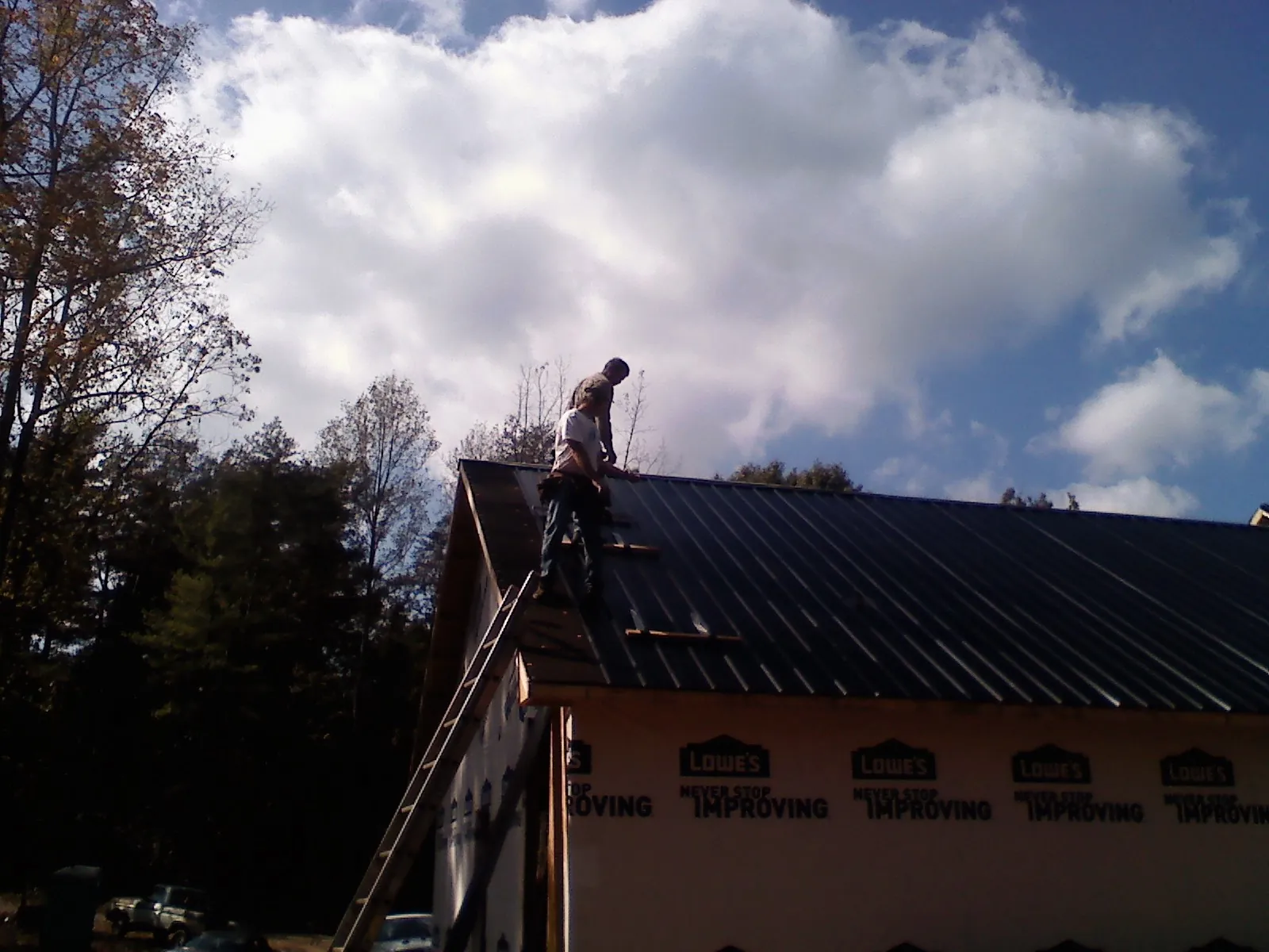 Roofer fastening dark metal panels high against a cloudy sky, from a Roof Inspection job in Hasty