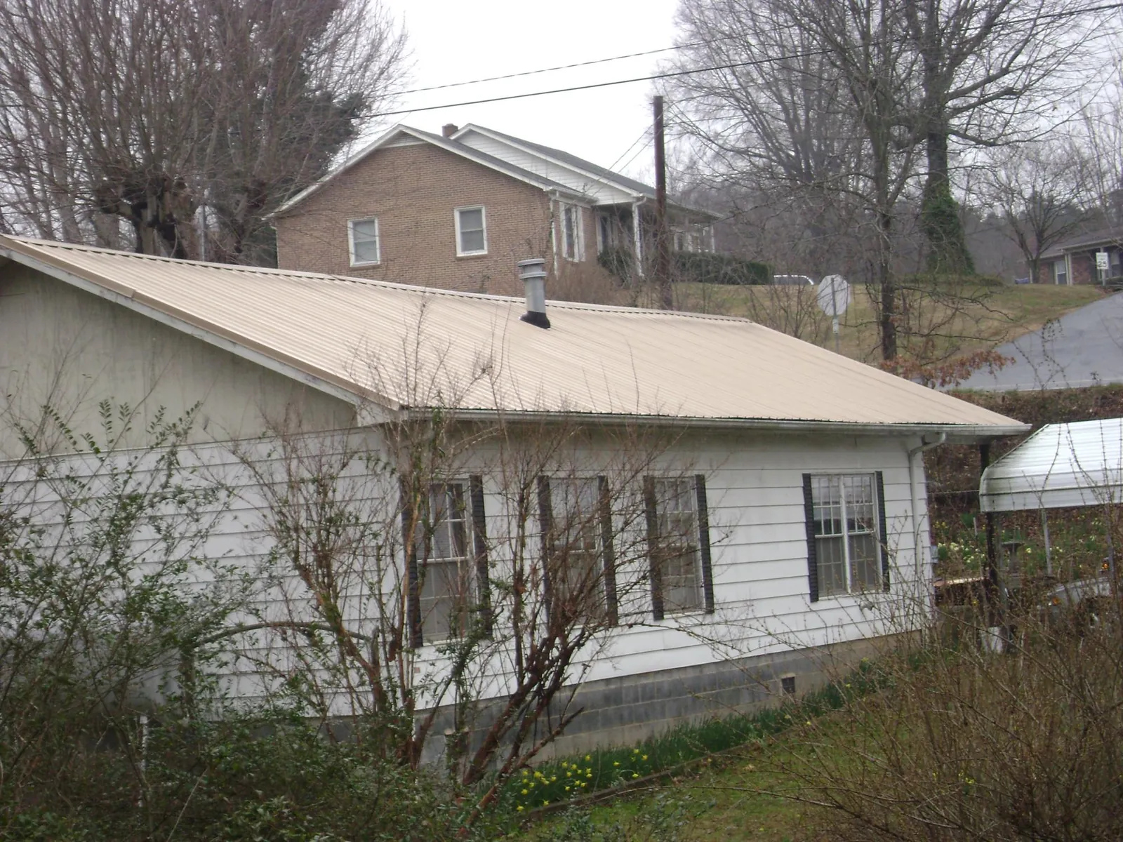 Tan metal roof on a white sided house set into a hillside — Commercial Roofing by Roofing Brothers in Hasty