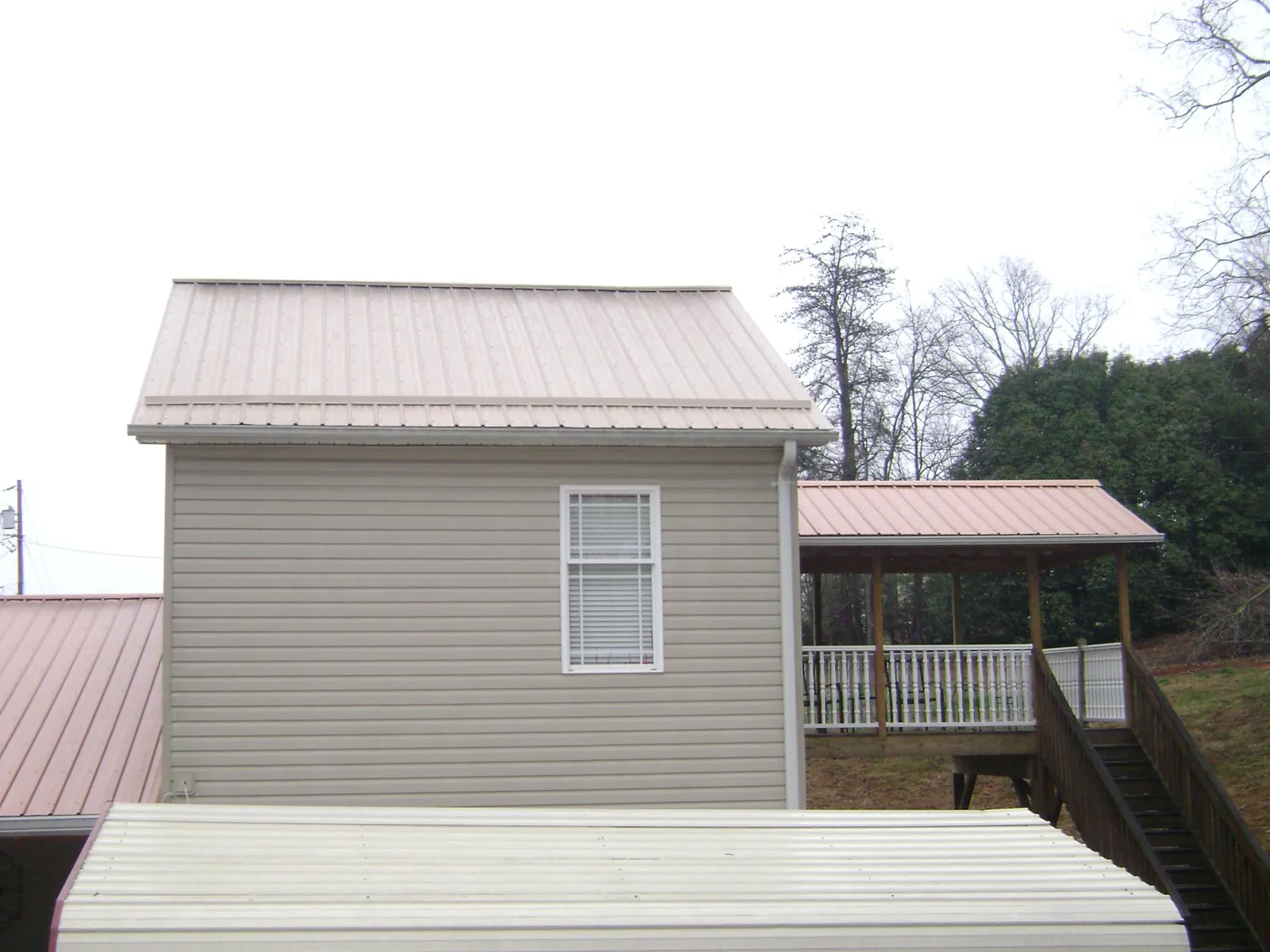 Tan metal roofs on a two story addition and attached porch, from a Roof Replacement job in Hasty