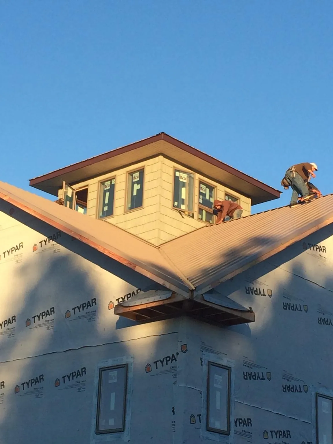 Roofers working around a rooftop cupola on a new metal roof at sunset — Roof Waterproofing in Hasty by Roofing Brothers